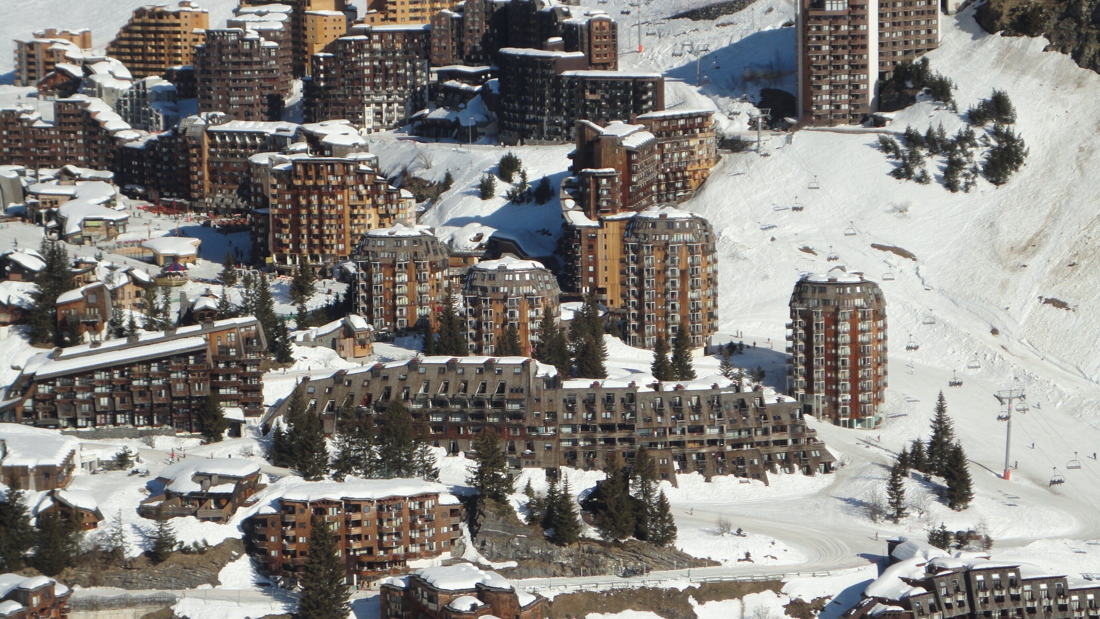 A snow-covered residential area with multiple apartment buildings, ski lifts, and a ski slope.
