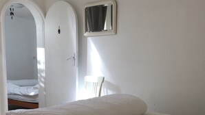 A bedroom with a bed, a chair, a mirror, and an air conditioning unit. - Small house, air conditioning and shaded garden, in a quiet area near the beach (Fleury)
