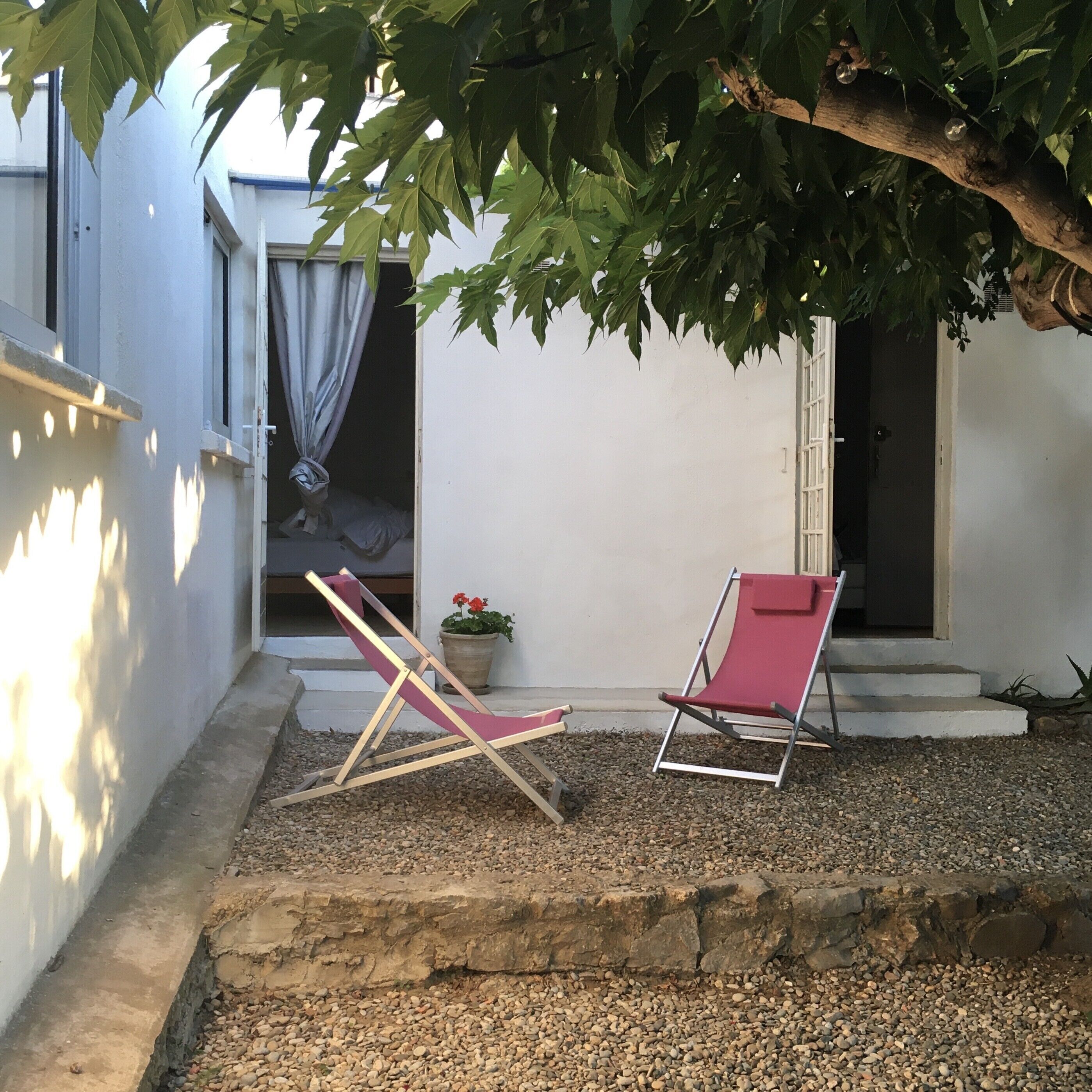 A small outdoor seating area with two red lounge chairs and a potted plant.