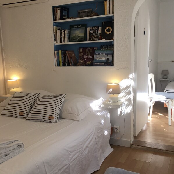 Un dormitorio con cama, dos lámparas de noche, una estantería llena de libros y una puerta que da a otra habitación.