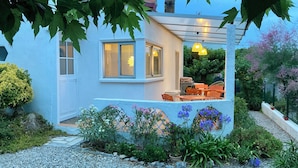 A modern house with a patio, outdoor seating, and a garden with various plants and flowers. - Small house, air conditioning and shaded garden, in a quiet area near the beach (Fleury)