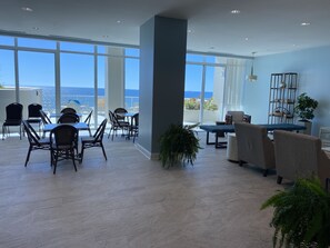 Relax in a spacious lounge area with a high ceiling and sea views, featuring comfortable seating and potted plants.