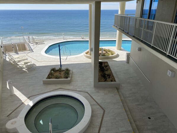 Relax by the pool and hot tub, surrounded by lounge chairs and sunbeds, with a balcony offering ocean views.