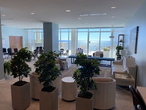 Relax in a stylish lounge area with sofas, chairs, and a coffee table, surrounded by potted plants and offering ocean views.
