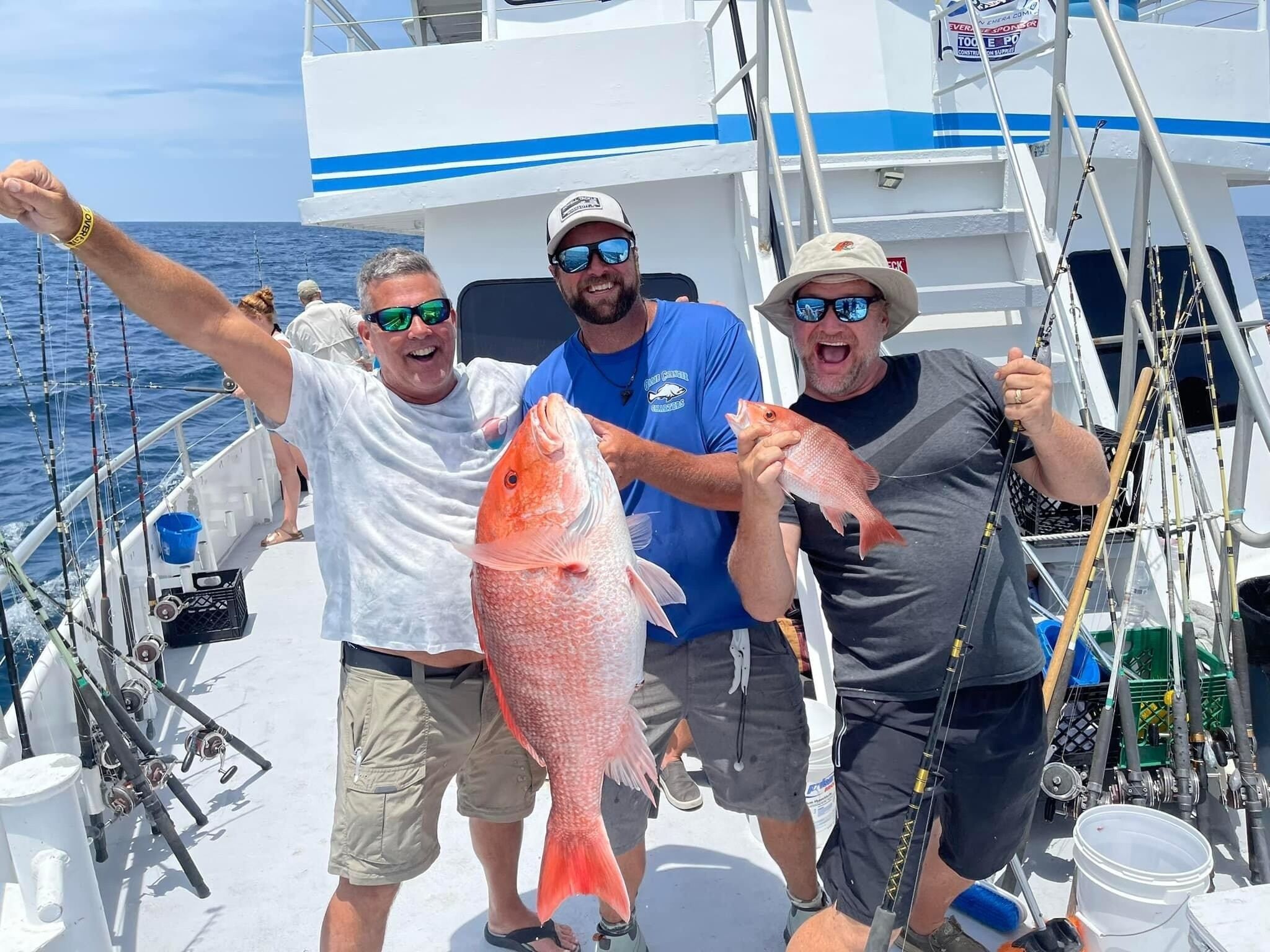 Three people on a boat holding fish, with fishing rods and equipment visible.
