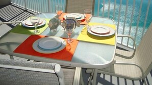 Une table dressée pour deux personnes, avec des assiettes, des verres et un menu, sur un balcon donnant sur la mer.