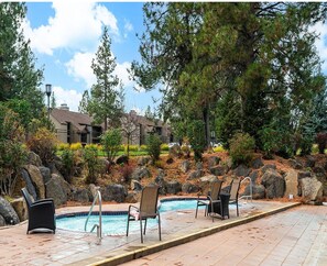 A swimming pool with lounge chairs, surrounded by rocks and trees, with a building in the background.