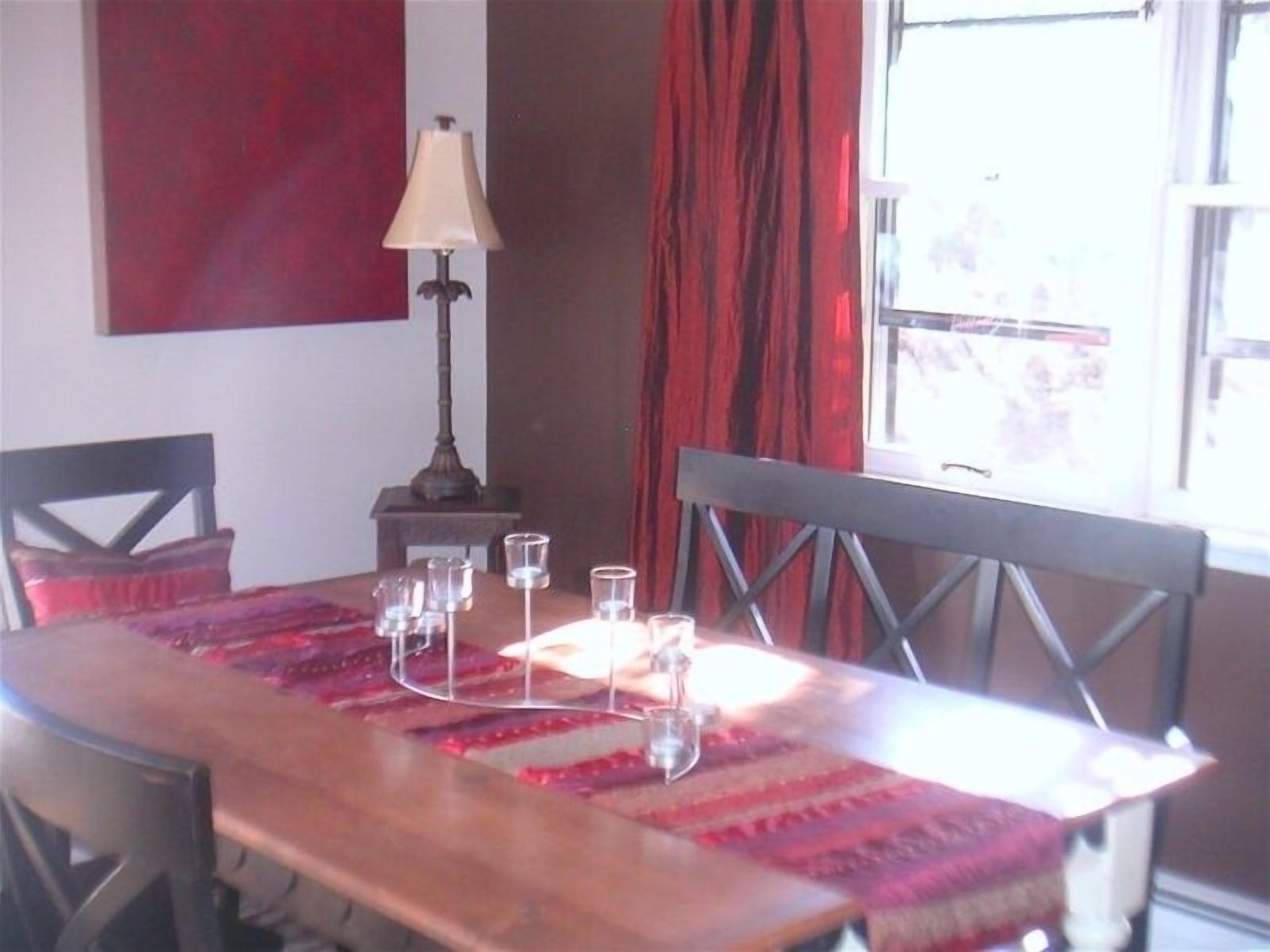 Una mesa de comedor con mantel rojo, una lámpara y varios vasos.