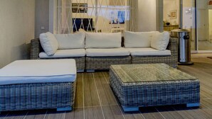 Un salon moderne avec un canapé d’angle, deux poufs et une cloison en verre.