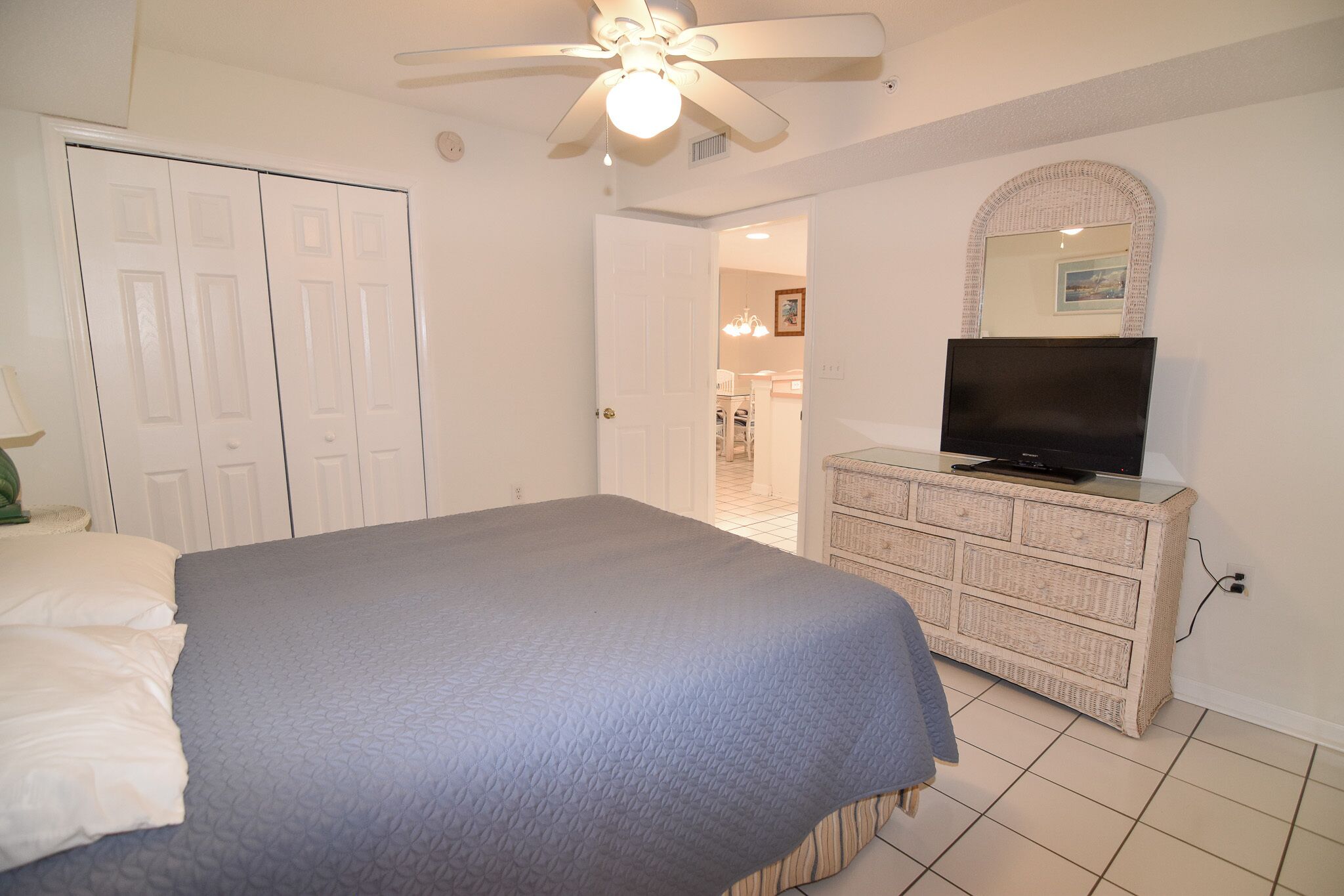A bedroom with a bed, a dresser, a television, and a ceiling fan.