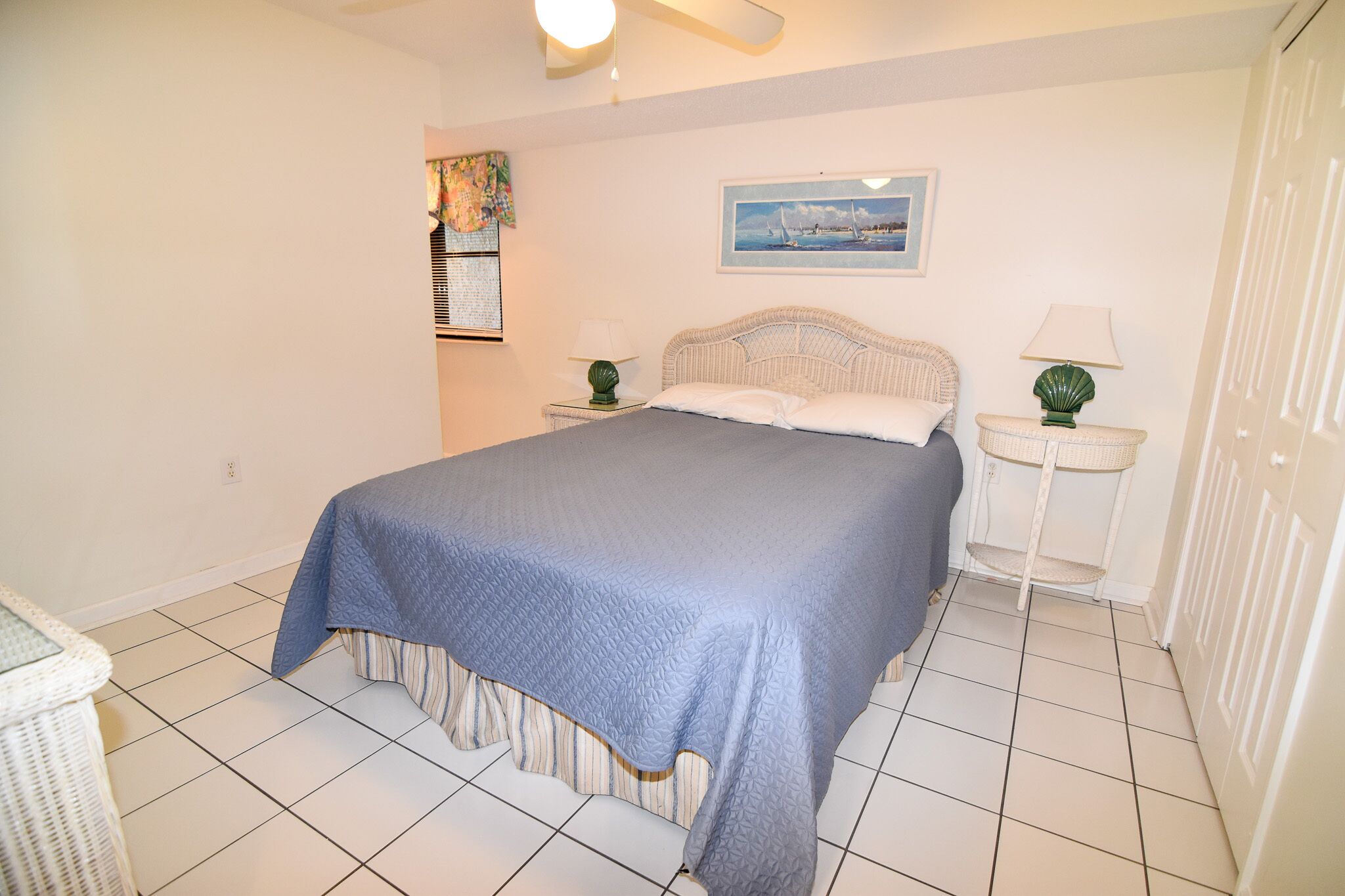 A neatly arranged bedroom with a bed, two bedside tables, a wall-mounted artwork, and a tiled floor.