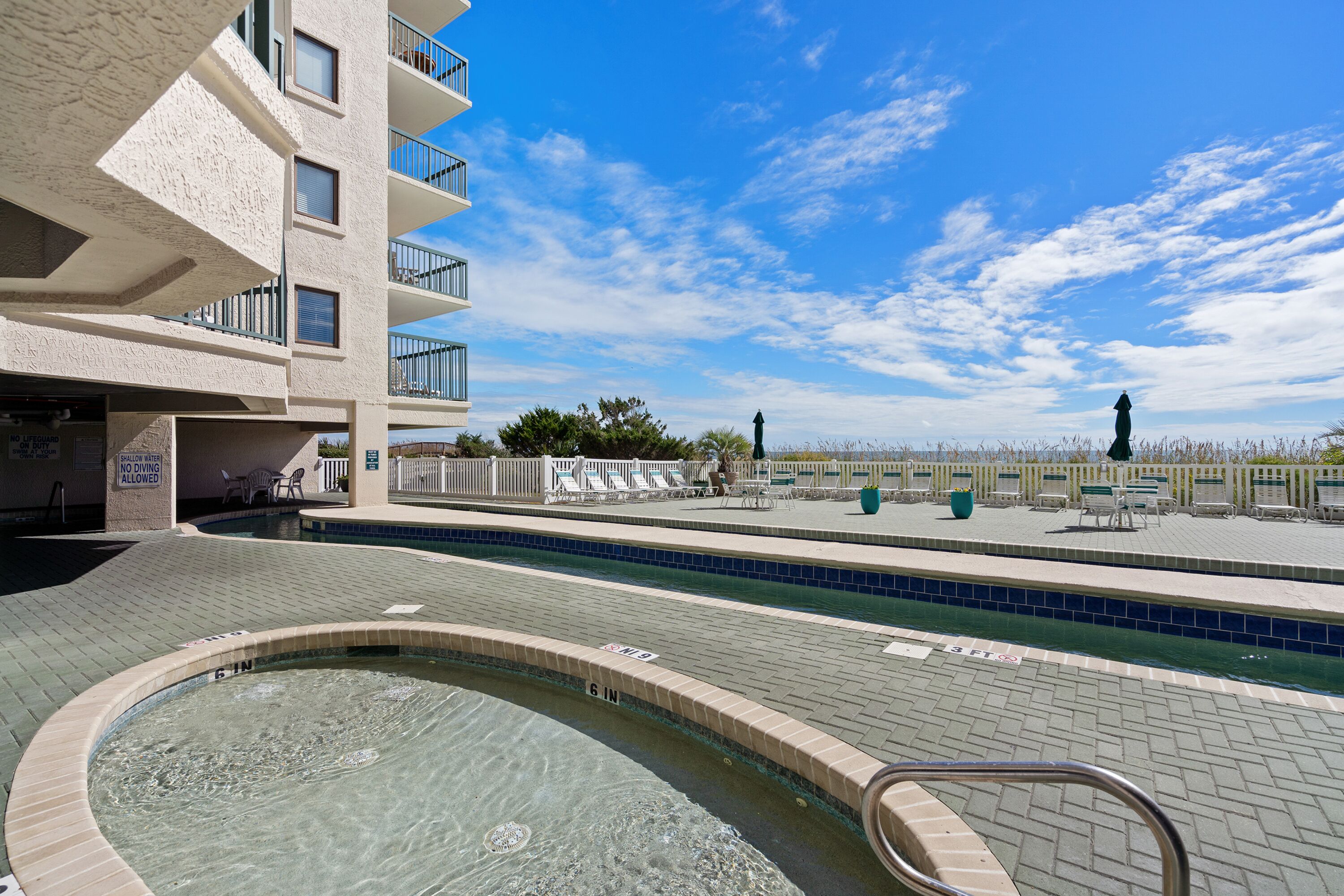 A swimming pool area with a hot tub, lounge chairs, and a view of the ocean.