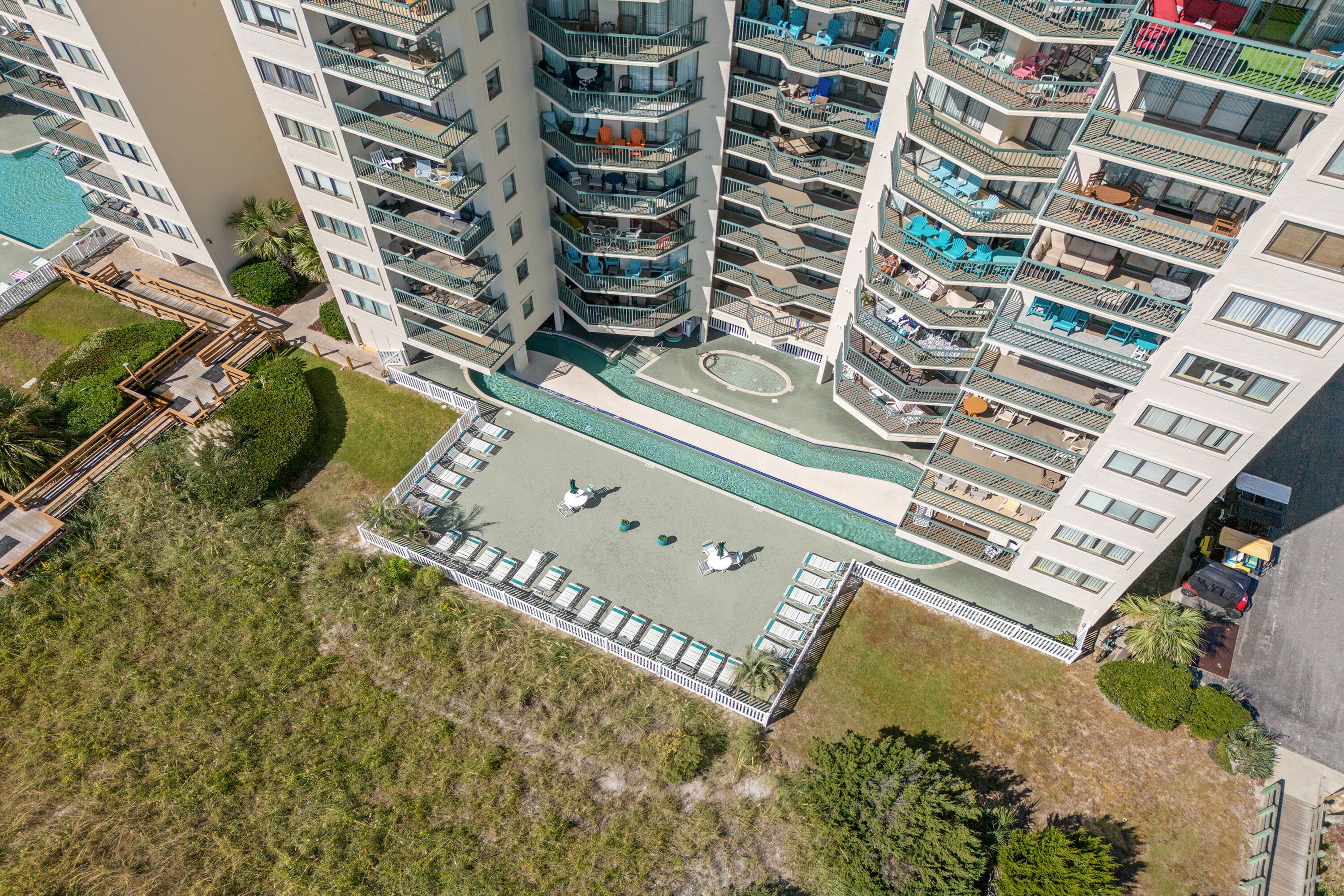 A high-rise building with multiple balconies, a swimming pool, and a rooftop deck with lounge chairs.