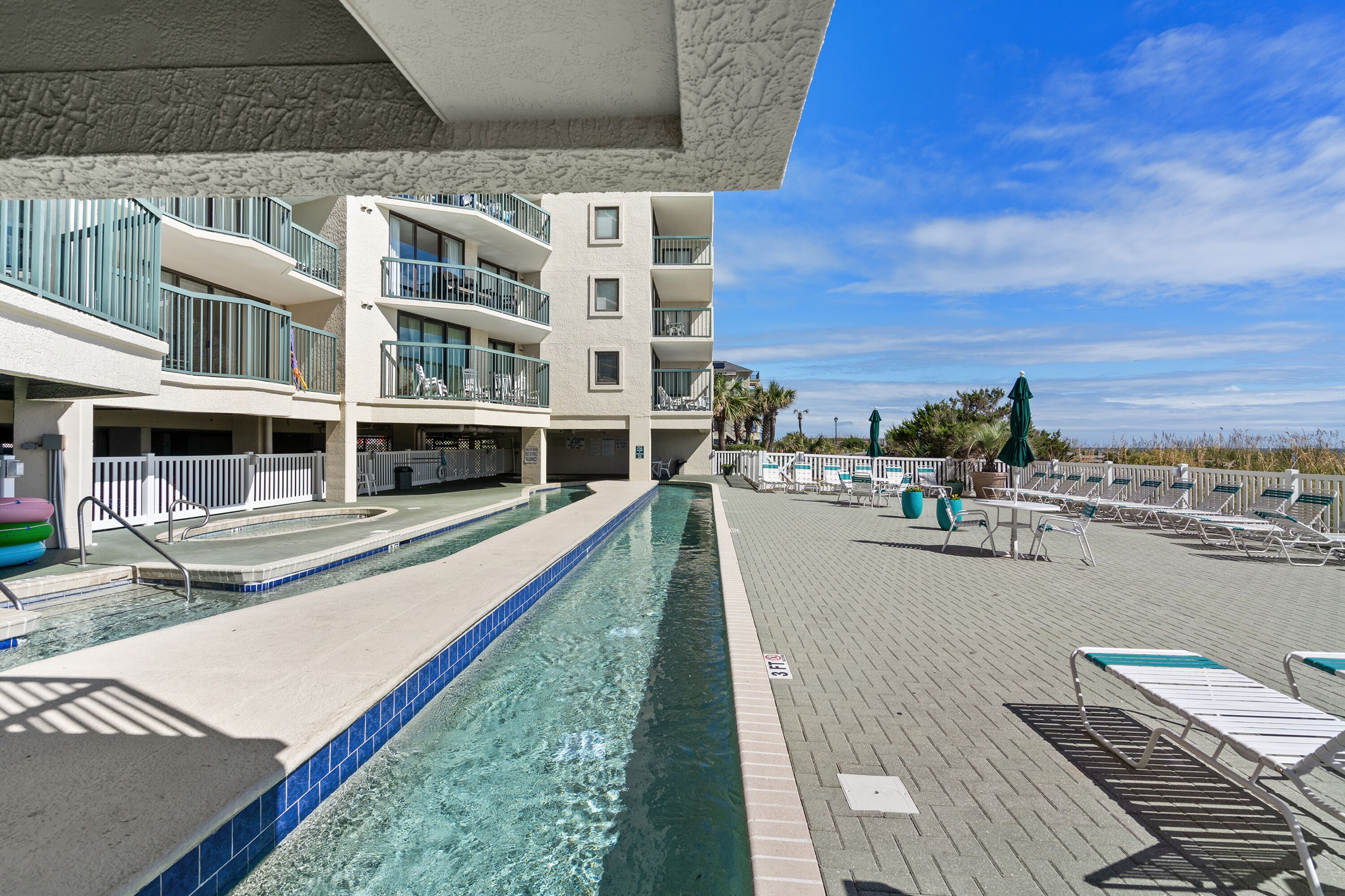 Zona de piscina amb una piscina blava cristal·lina, gandules i vista a l'oceà.