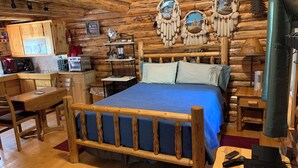 A log cabin-style room with a wooden bed, a desk, a chair, and a small kitchenette. - Sha Bear Cabin, on the YAAK RIVER~Quiet, Romantic Cabin Sleeps up to 4 (Troy)