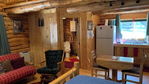 A cabin interior with a wooden interior, a dining area, a kitchen with a sink, and a toilet. - Sha Bear Cabin, on the YAAK RIVER~Quiet, Romantic Cabin Sleeps up to 4 (Troy)