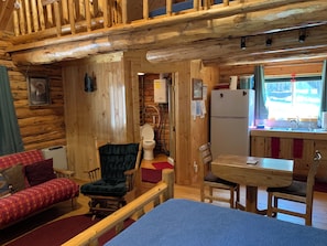 A cabin interior with a wooden interior, a dining area, a kitchen with a sink, and a toilet.