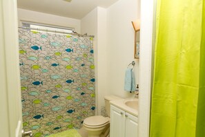 A bathroom with a shower curtain featuring a fish pattern, a toilet, a sink with a soap dispenser, and a towel hanging on a rack. - Comfortable Beach Cottage, just 1 mile to Bethany Beach! Community Pool, Tennis, Beaches! (Frankford)