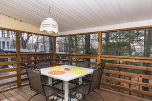 A covered outdoor seating area with a table and chairs, surrounded by wooden railings and a view of trees and buildings. - Comfortable Beach Cottage, just 1 mile to Bethany Beach! Community Pool, Tennis, Beaches! (Frankford)