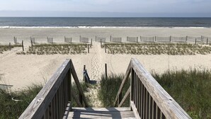 A wooden boardwalk leading to a sandy beach with a fence and chairs. - Oceanfront Home (Holden Beach)