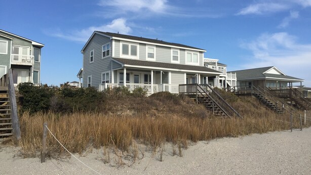 A beachfront property with multiple-story houses, a sandy beach, and a clear sky. - Oceanfront Home (Holden Beach)