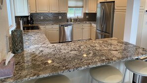 Una cocina moderna con armarios blancos, un refrigerador de acero inoxidable y una encimera de granito.