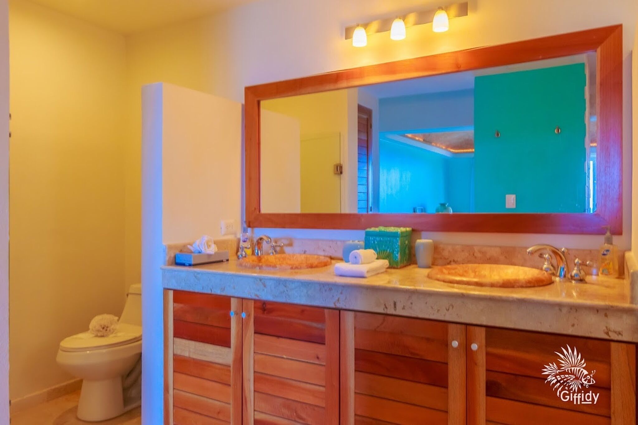 Une salle de bain avec un meuble-lavabo en bois, un grand miroir et des toilettes.