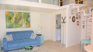Un salon moderne avec un canapé bleu, une table basse en verre et des œuvres d’art abstraites accrochées au mur.