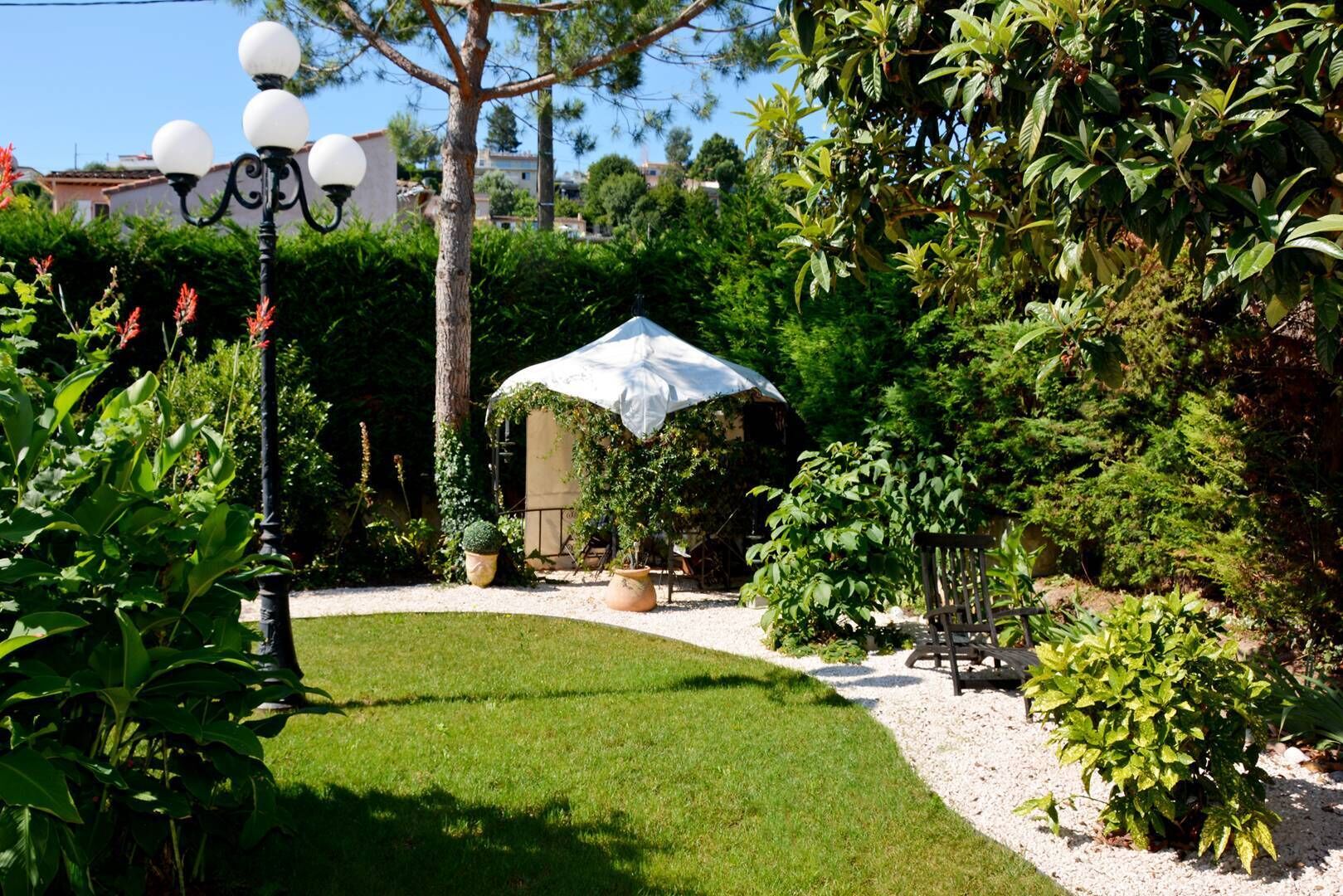 Un jardin bien entretenu, avec une pelouse, des plantes en pot et une pergola recouverte d’un tissu blanc.