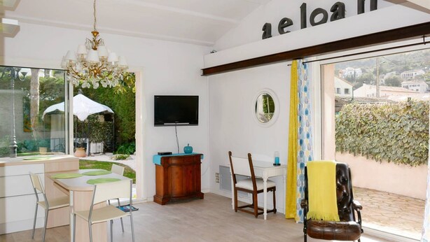 Un salon moderne comprenant un coin repas, un téléviseur fixé au mur et une grande fenêtre donnant sur l’extérieur.