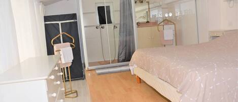 Une chambre à coucher comprenant un lit, un miroir, une armoire et un espace douche.