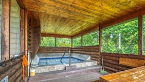 Una cabaña de madera con jacuzzi, terraza de madera y vistas al bosque.
