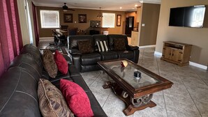 A living room with a leather sofa, a glass coffee table, and a flat-screen TV mounted on the wall.