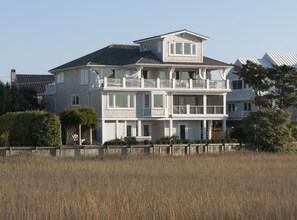 A two-story house with a balcony on the second floor, a garage, and a front yard with a fence. - Coastal Oasis with Panoramic Water Views ~ Wrightsville Beach (Wrightsville Beach)