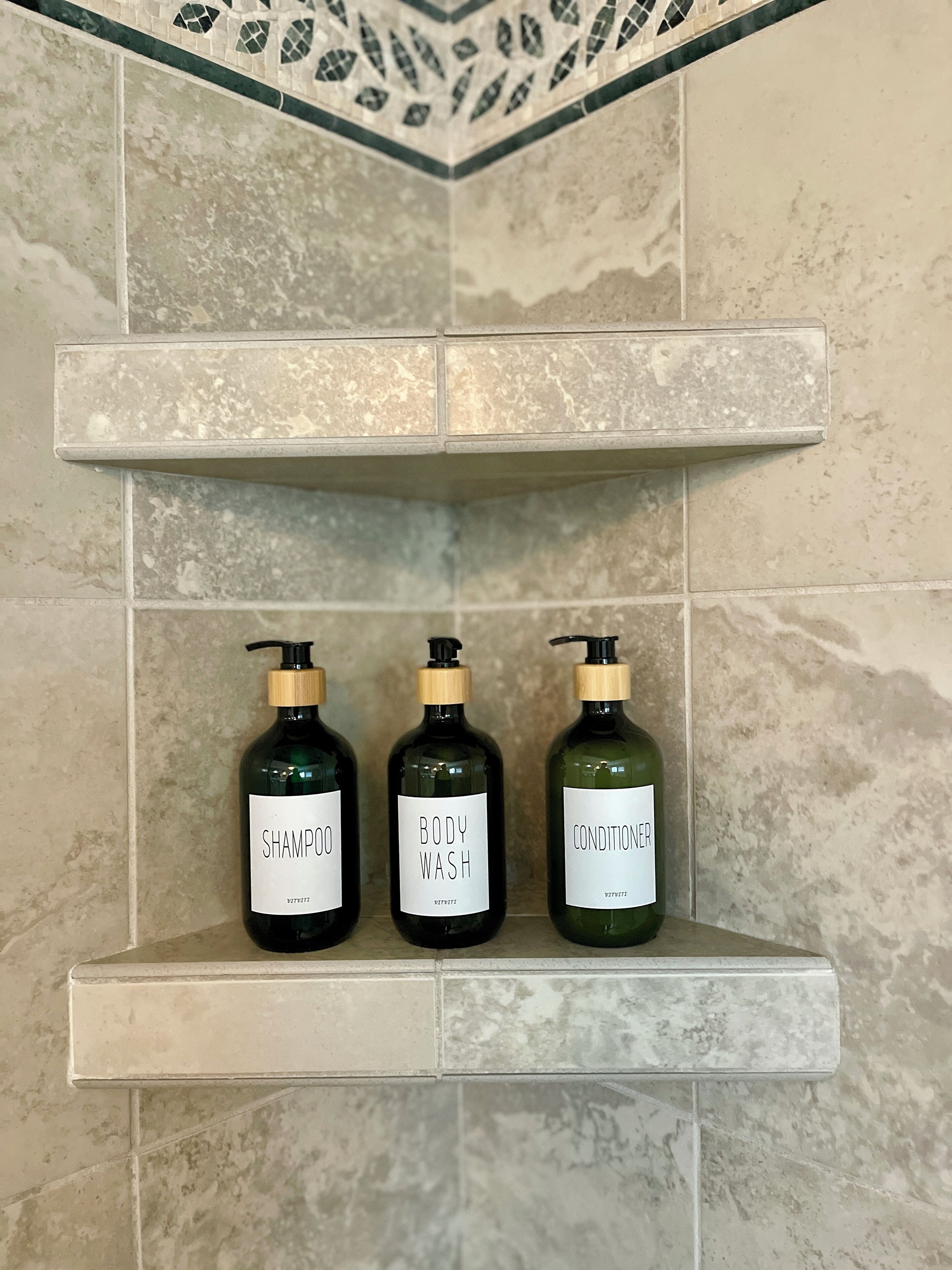 A bathroom shelf with three bottles of toiletries: shampoo, body wash, and conditioner.