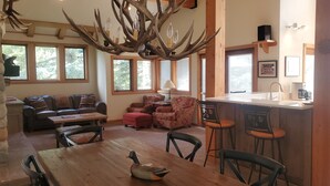 A spacious living room with a wooden dining table, leather sofas, and a unique antler chandelier. - Sage Haven Welcomes EIGHT to TEN Guests. Let the Sun Valley Adventures Begin! (Ketchum)