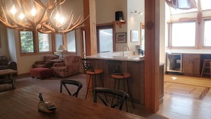 A spacious living room with a wooden dining table, a chandelier, and a kitchen area with a bar. - Sage Haven Welcomes EIGHT to TEN Guests. Let the Sun Valley Adventures Begin! (Ketchum)