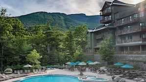 A resort with a swimming pool, lounge chairs, and umbrellas, surrounded by lush greenery and mountains. - 1117 | Studio | The Mansfield | 1st floor | Private Wooded Mountain Views (Stowe)