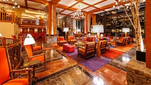 A spacious lobby with a stone fireplace, wooden furniture, and a large chandelier. - 1117 | Studio | The Mansfield | 1st floor | Private Wooded Mountain Views (Stowe)