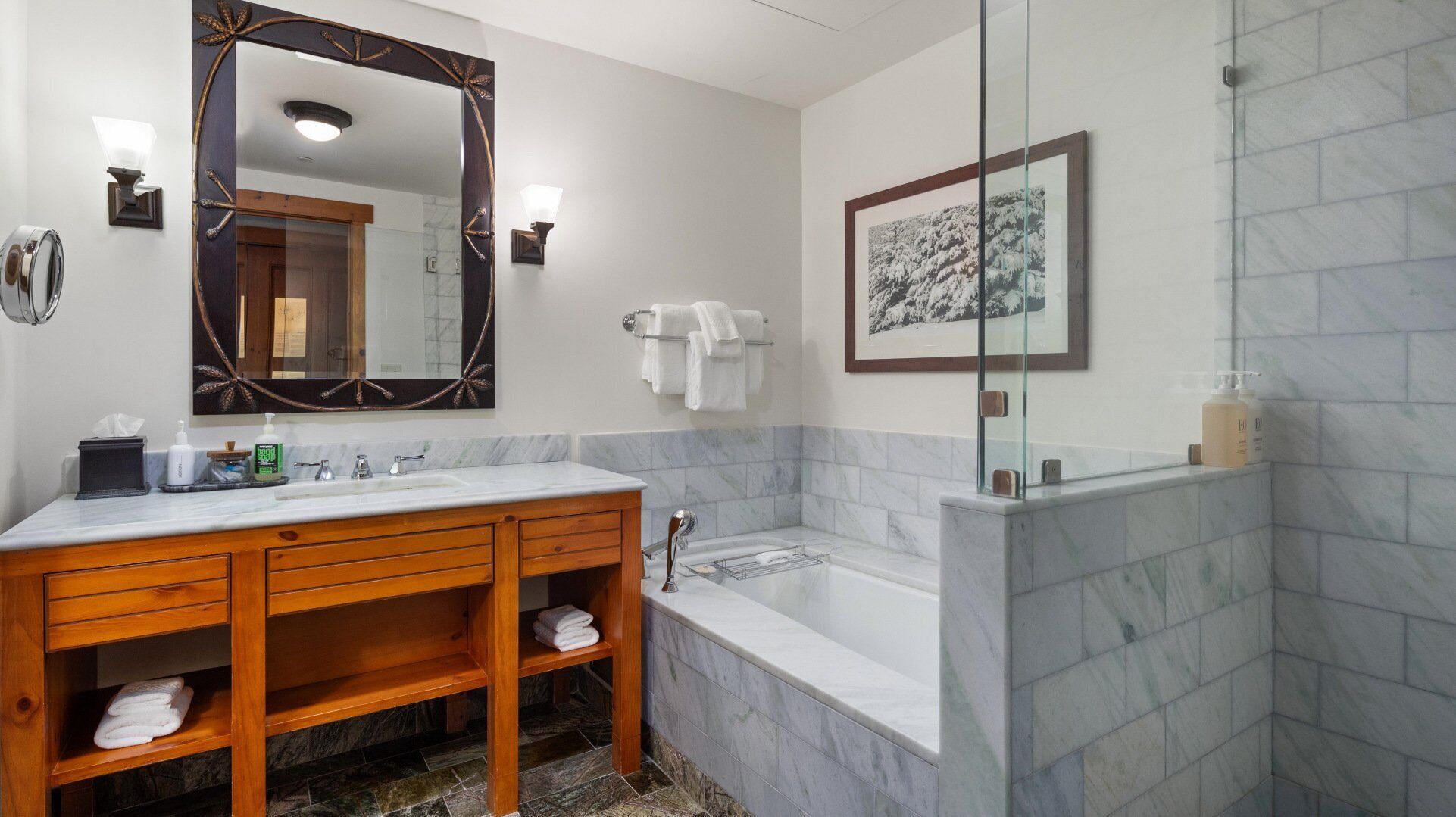Une salle de bain avec un lavabo en marbre, un meuble-lavabo en bois, un grand miroir, une baignoire et une cabine de douche en verre.