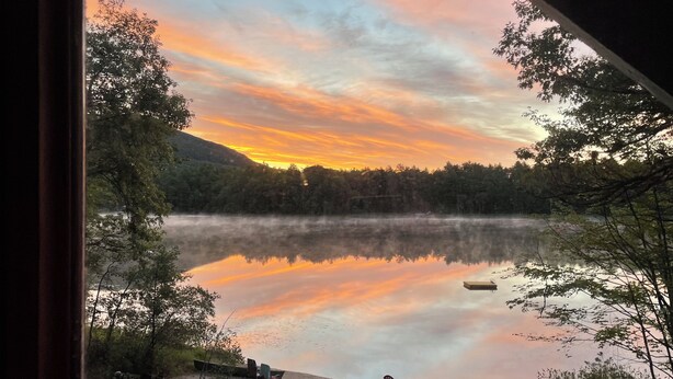 Ein friedlicher See bei Sonnenuntergang, ruhiges Wasser spiegelt den Himmel wider, mit Außenplätzen am Ufer.