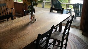 Ein Holztisch mit Stühlen, eine Vase mit gelben Blumen und Blick auf einen See durch große Fenster.