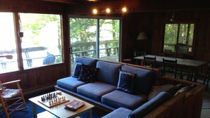 Ein gemütliches Wohnzimmer mit einer Couch, einem Couchtisch mit einem Schachspiel und großen Fenstern, die einen Blick ins Freie bieten.