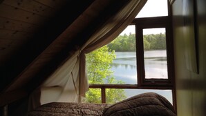 Ein Schlafzimmer mit großem Fenster und Blick auf einen See und Bäume.