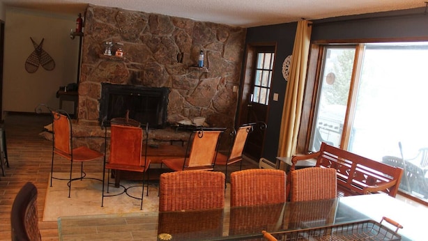 Uma sala de estar aconchegante com lareira de pedra, móveis de vime e uma mesa de vidro.