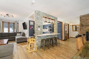 Ein modernes Wohnzimmer mit einer Steinwand, einer Bar mit Hockern, einer Couch und einem Kamin.