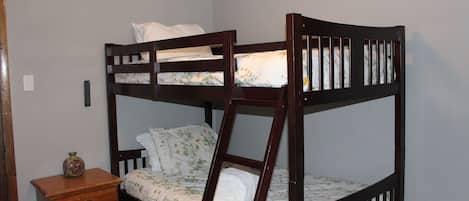 A bunk bed with a ladder, a bedside table with a vase, and a wall switch.
