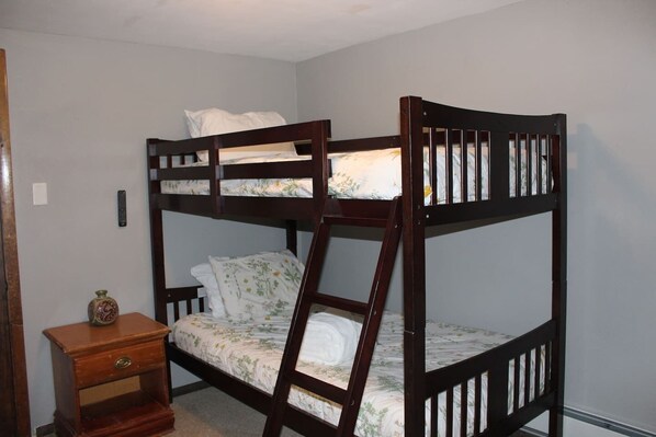 A bunk bed with a ladder, a bedside table with a vase, and a wall switch.