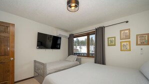 Quarto com uma cama, televisão, janela com cortinas e porta.
