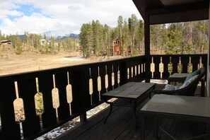 A wooden deck with a table and chairs, overlooking a forest and distant mountains.